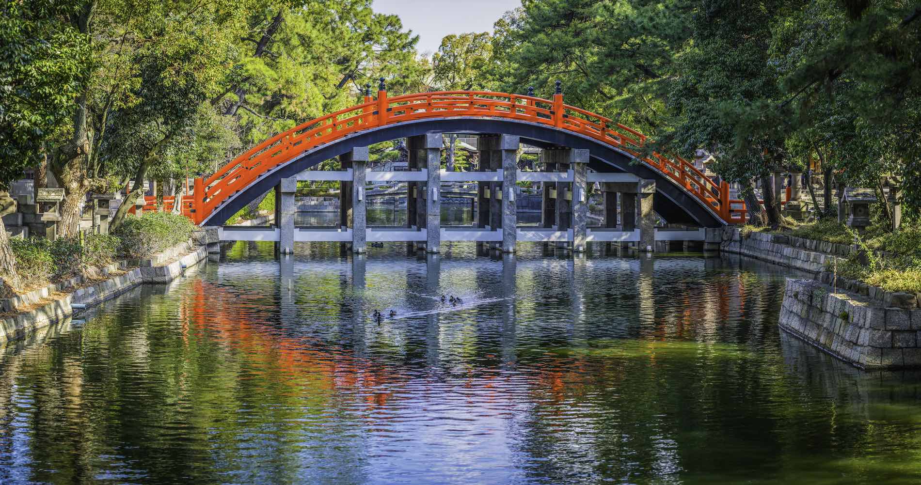 Traditional red wooden arch bridge over tranquil waterway in Sumiyoshi, Osaka, Japan's vibrant second city.
